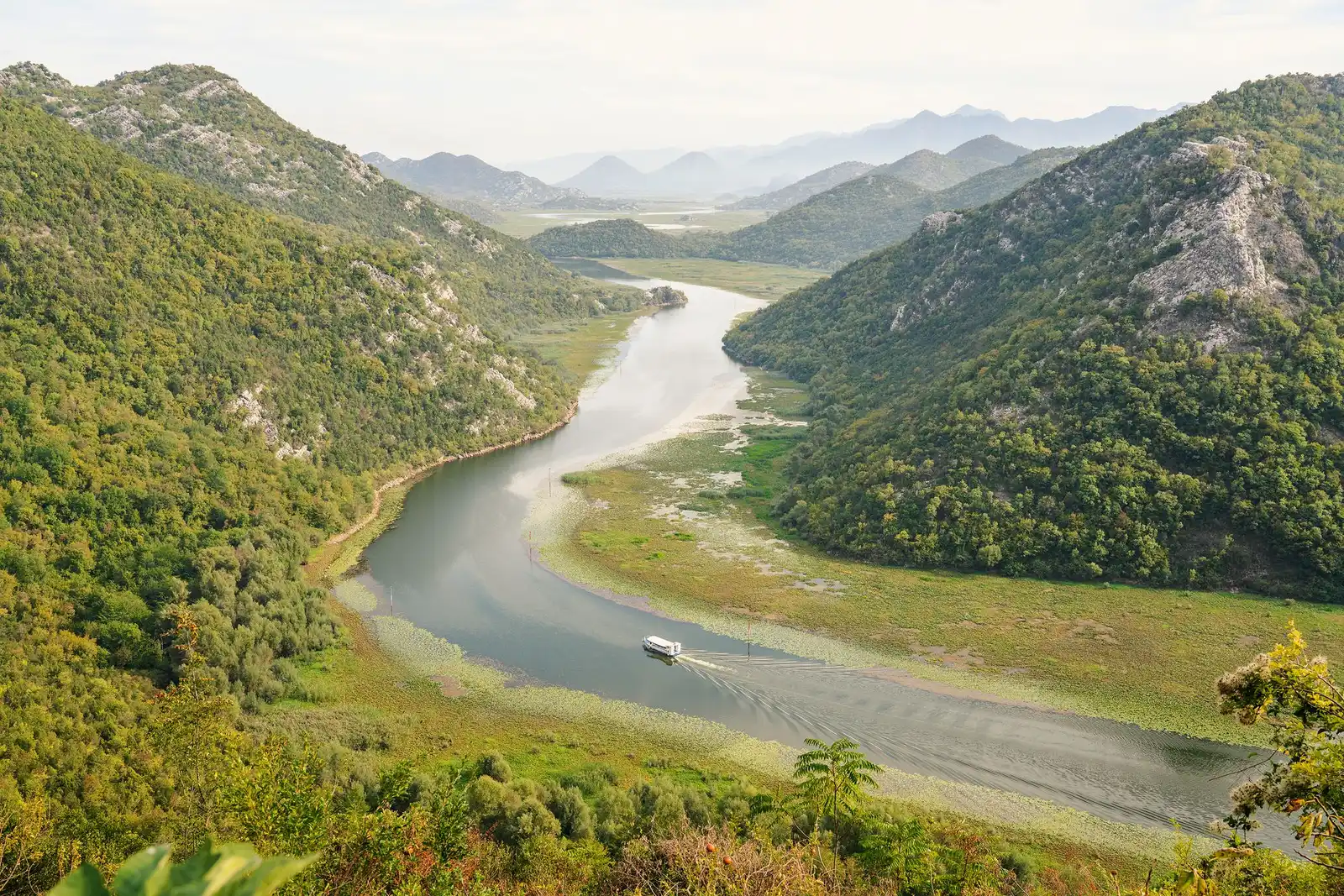 Zavoj Rijeke Crnojevića kroz zelena brda Skadarskog jezera, sa barkom na vodi